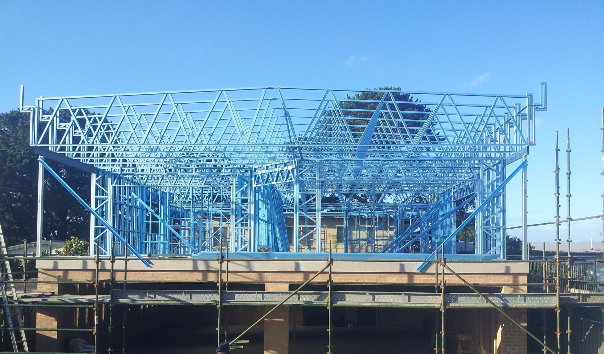 Blue steel frame of a building under construction, set against a clear blue sky.