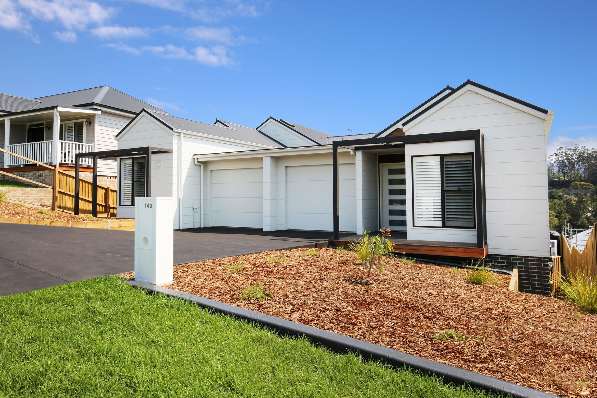 White houses with dark trim and garages, on a hillside with grass and mulch.