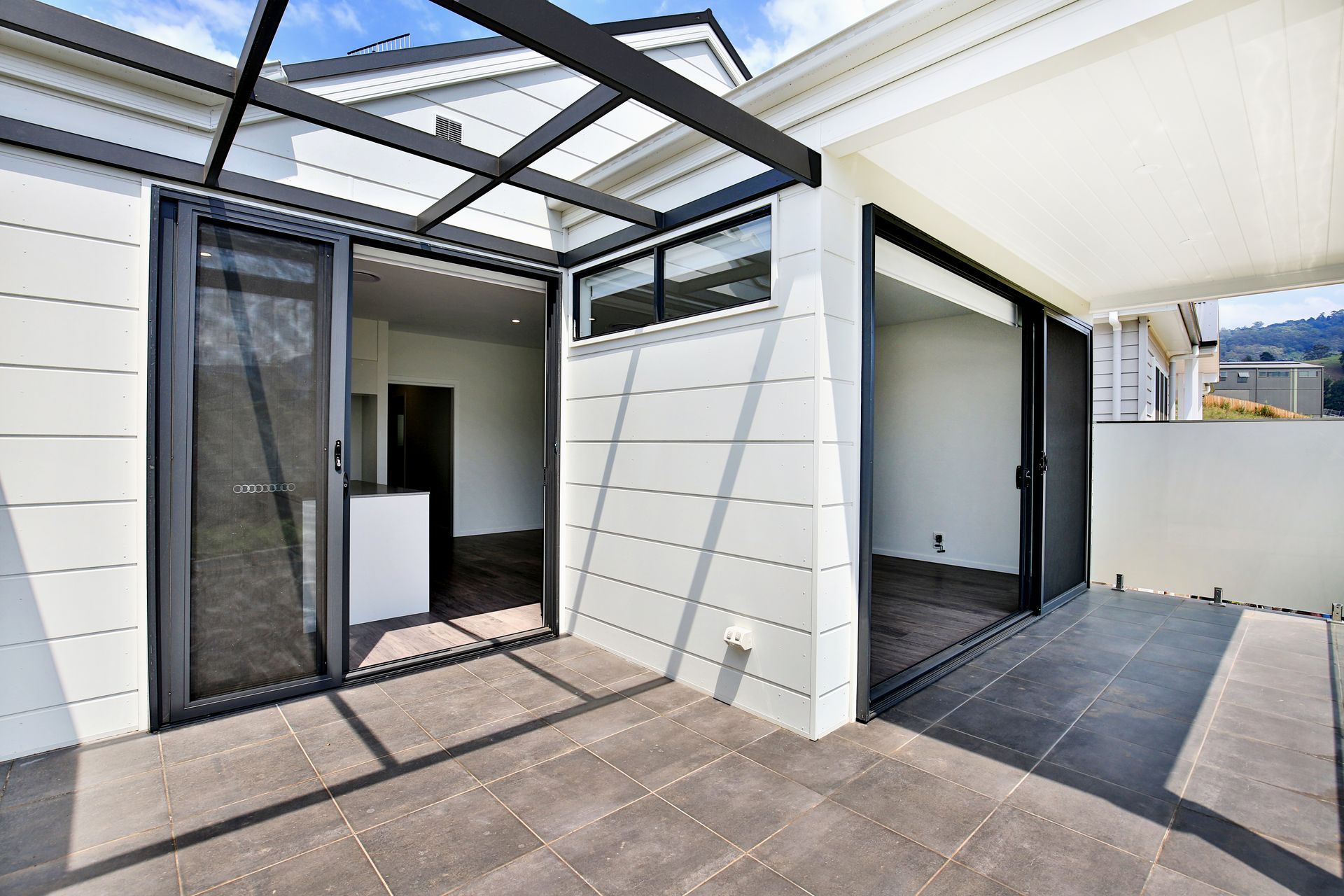 Exterior view of a modern balcony with sliding doors and a pergola, grey tile floor, white walls.