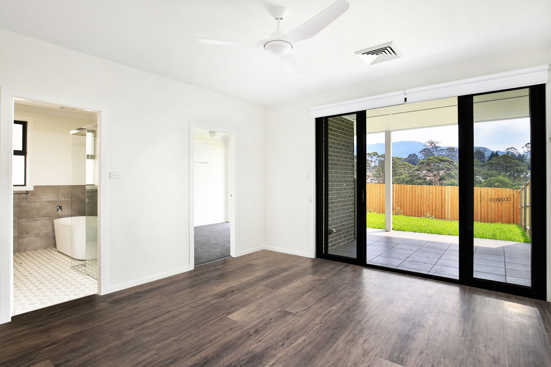 Empty room with wood floors, sliding glass doors to patio, and a view of trees and mountains.
