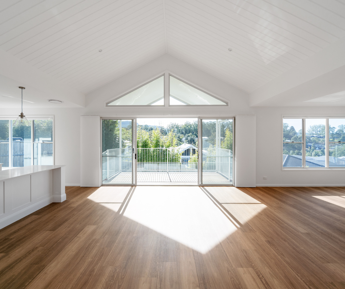 Bright empty living room with vaulted ceiling, wood floors, and large sliding glass doors to a balcony.