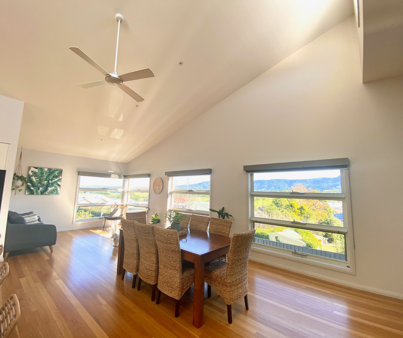 Bright dining room with wood floors, wicker chairs, and large windows overlooking a scenic landscape Bright dining room with wood floors, wicker chairs, and large windows overlooking a scenic landscape