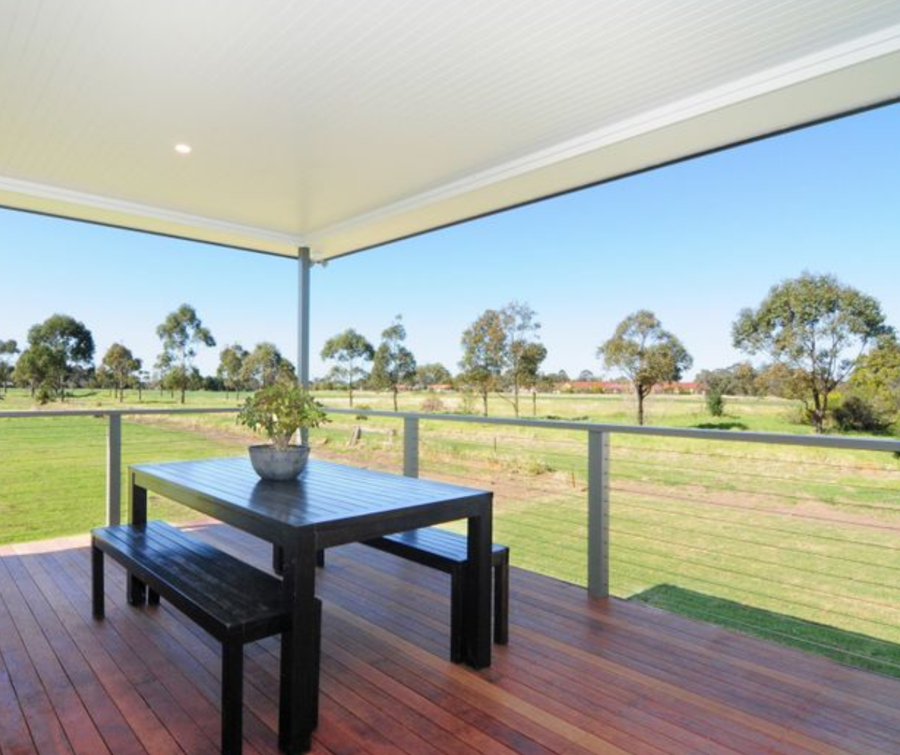 Covered deck with black table and benches overlooking a grassy field and trees under a blue sky Covered deck with black table and benches overlooking a grassy field and trees under a blue sky