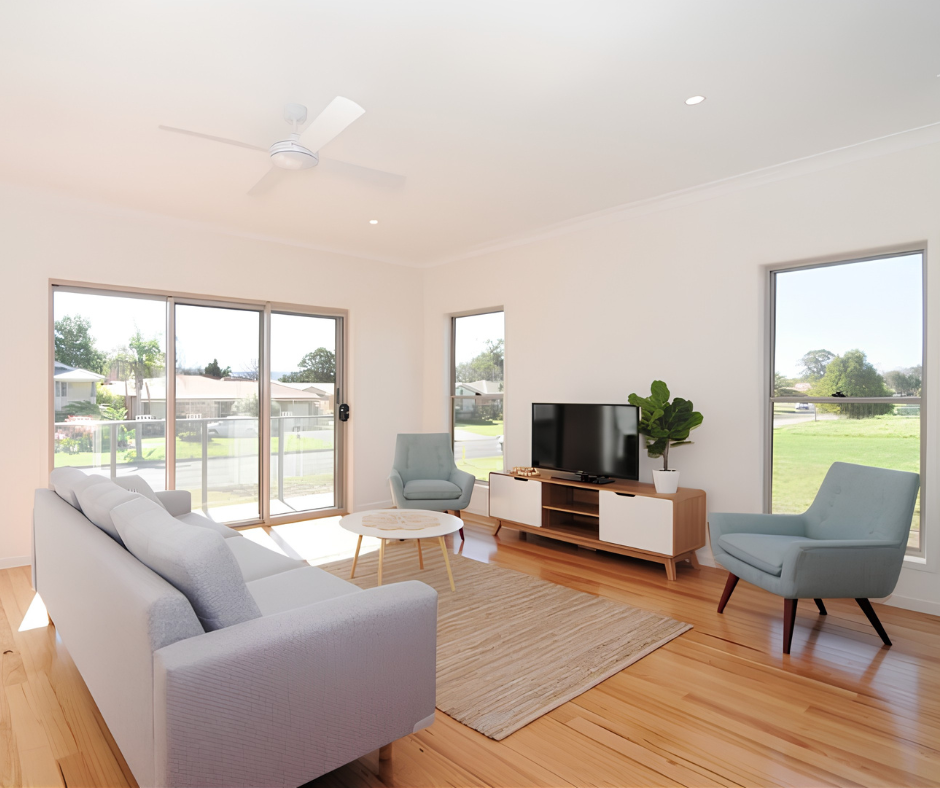 Bright modern living room with gray sofa, blue chairs, TV stand, and sliding doors to a backyard view