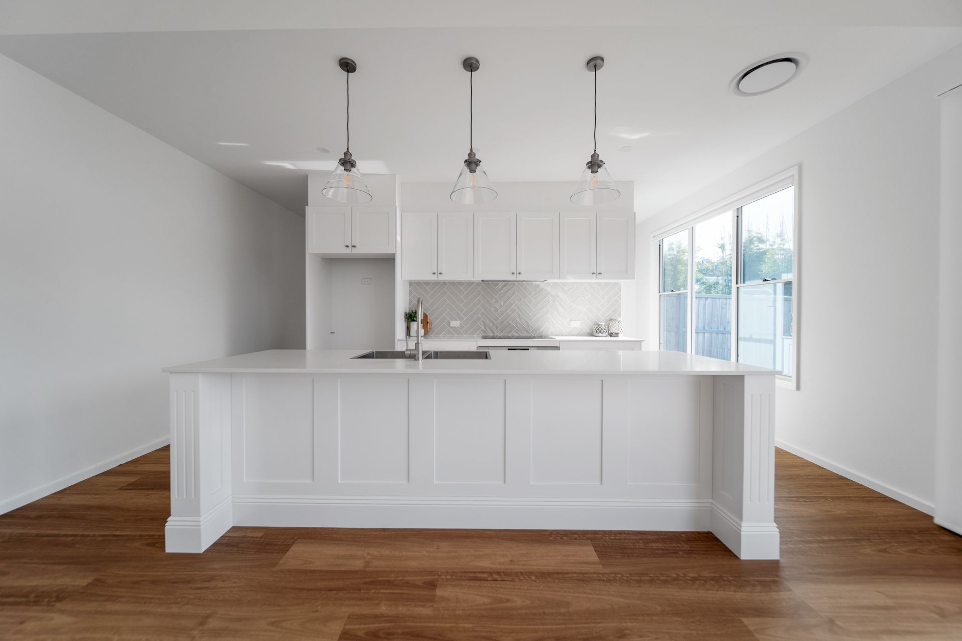 White kitchen with island, cabinets, pendant lights, wooden floor, and a window.