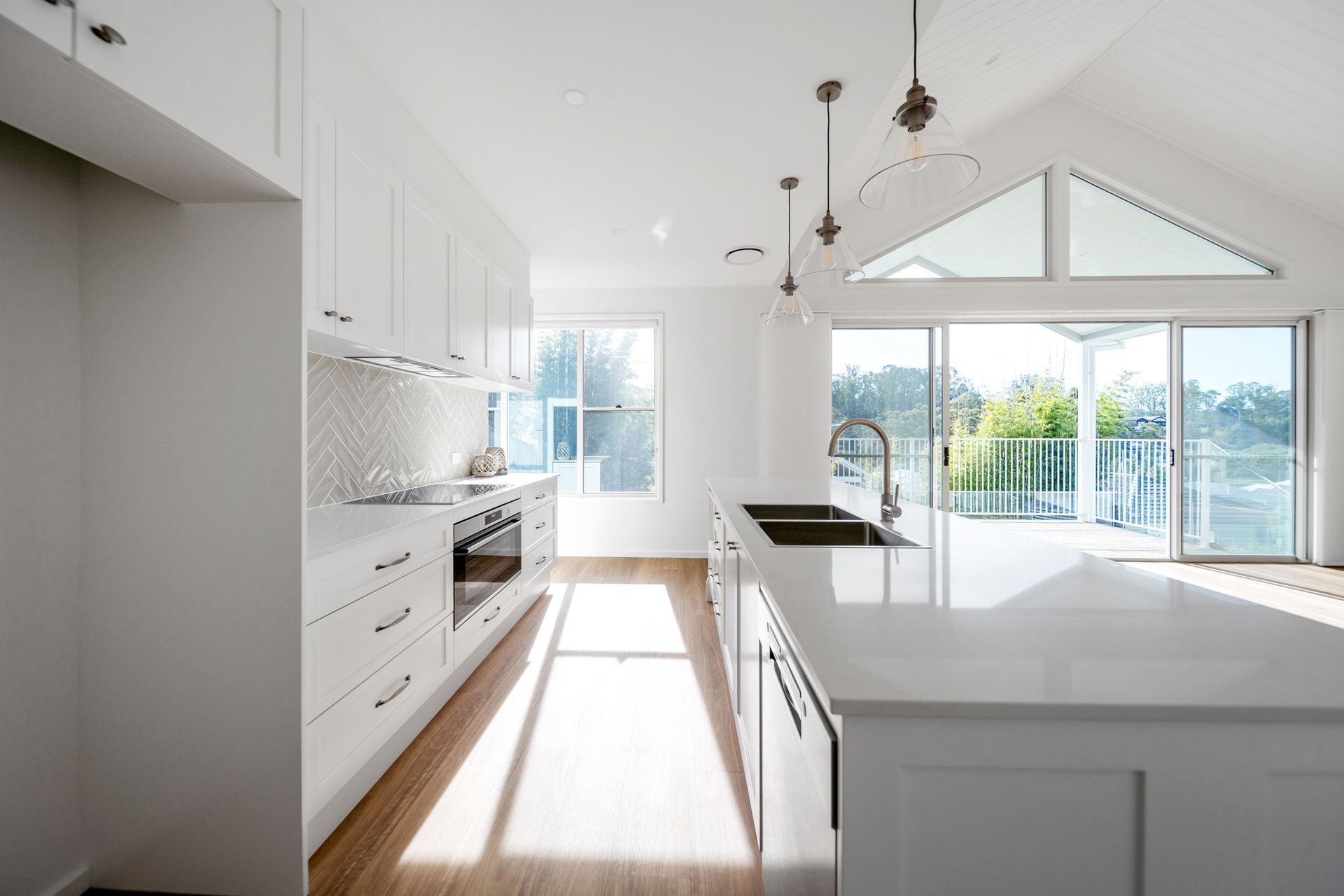 White kitchen with island, cabinets, and large windows. Bright, airy space with light wood flooring.