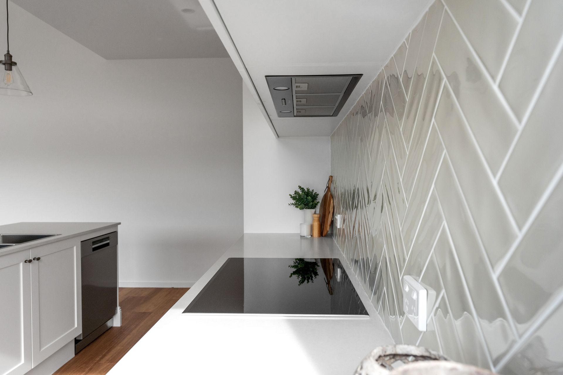 Modern kitchen with white countertops, herringbone tile backsplash, and built-in stovetop.