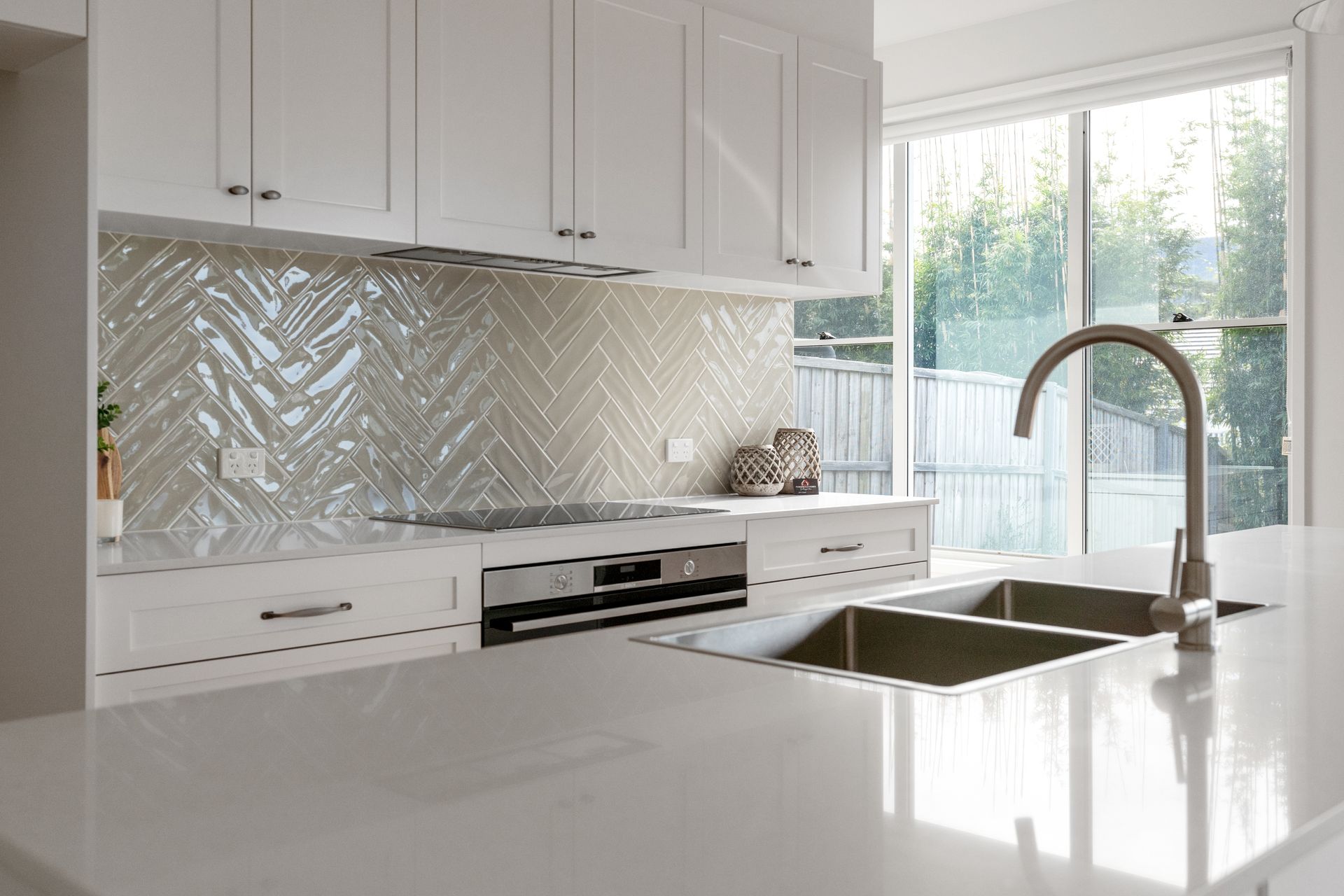 White kitchen with backsplash, cabinets, and sink in front of a window.