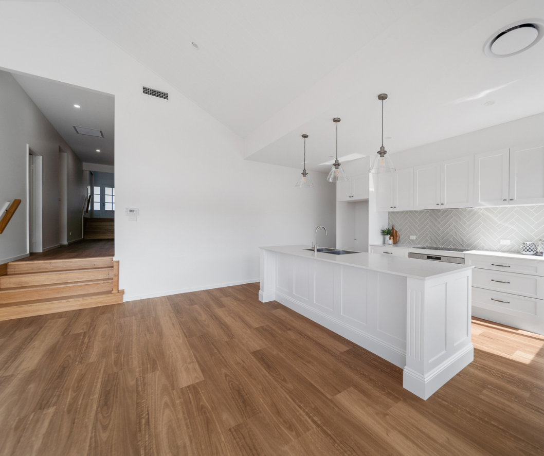 Bright modern kitchen with white cabinets, wood floors, island, and adjacent staircase hallway Bright modern kitchen with white cabinets, wood floors, island, and adjacent staircase hallway