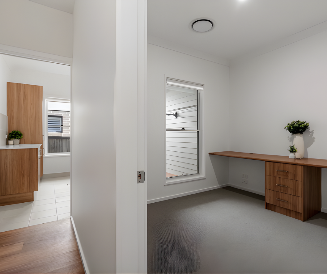 Bright modern room with a wooden desk, carpeted floor, and doorway to a kitchen beyond.