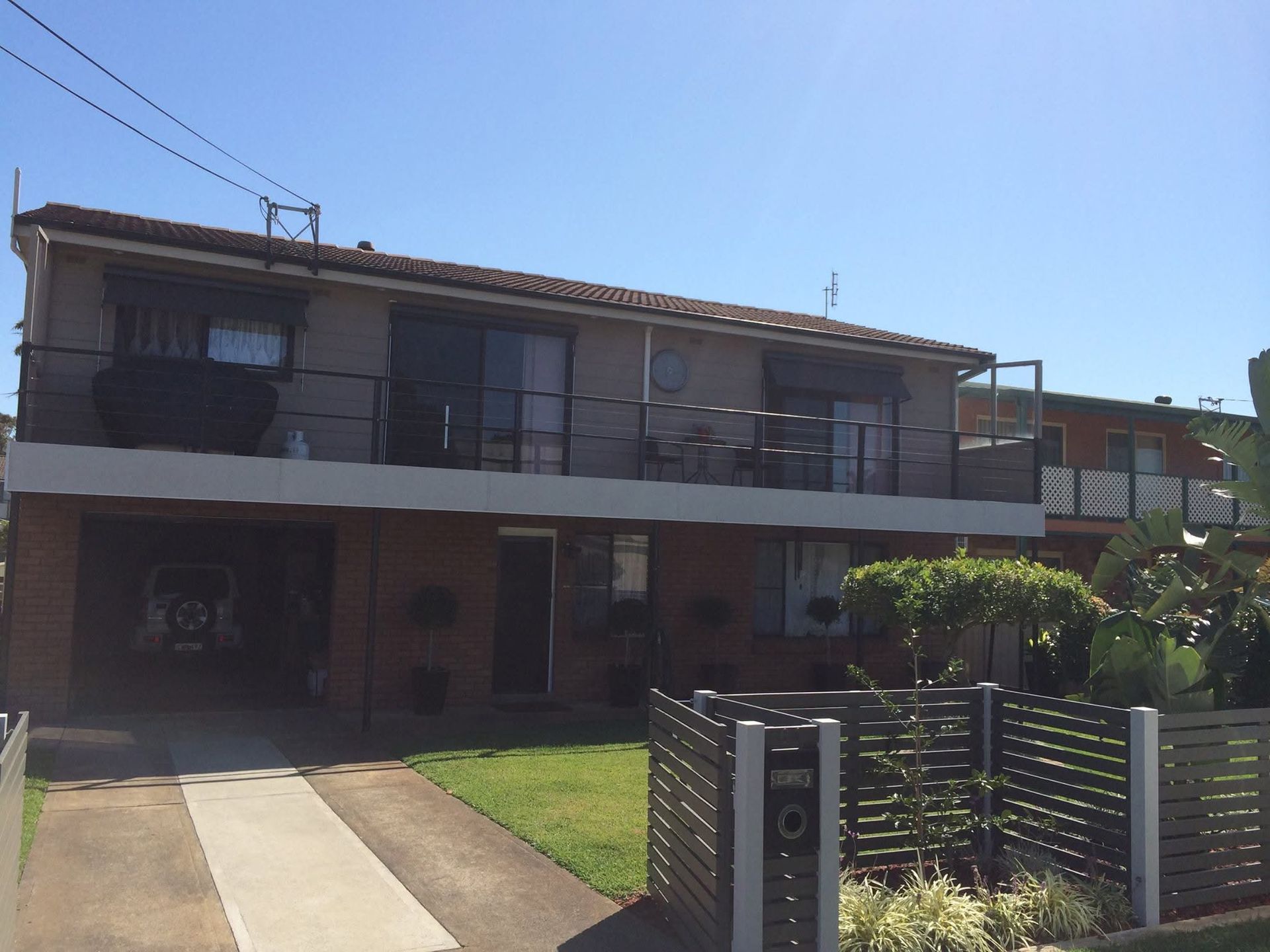 Two-story residential building with a driveway and small front yard. Black roller shutters and a black fence.