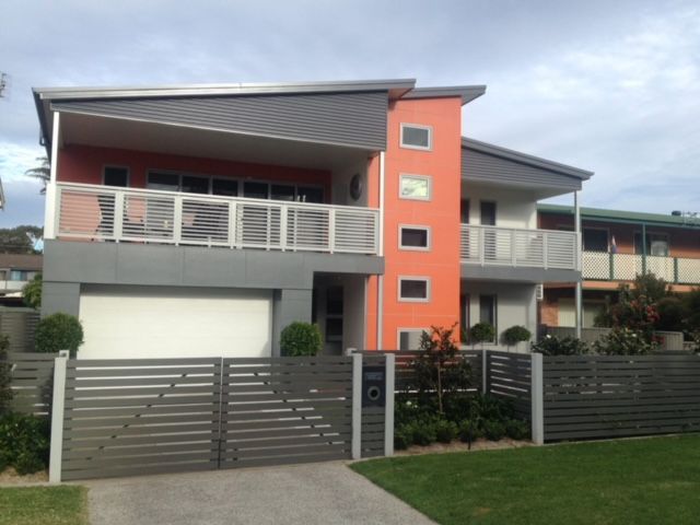 Modern two-story house with orange and gray accents, a white garage door, and a gray gate.