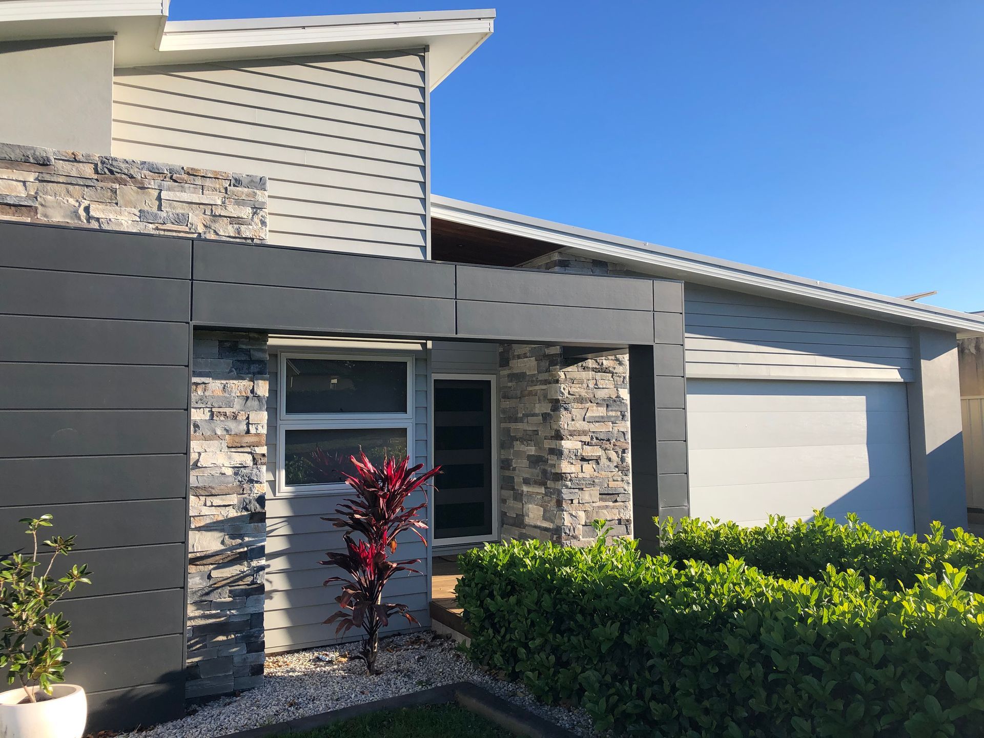 Modern home exterior with gray siding, stone accents, and a white garage door.