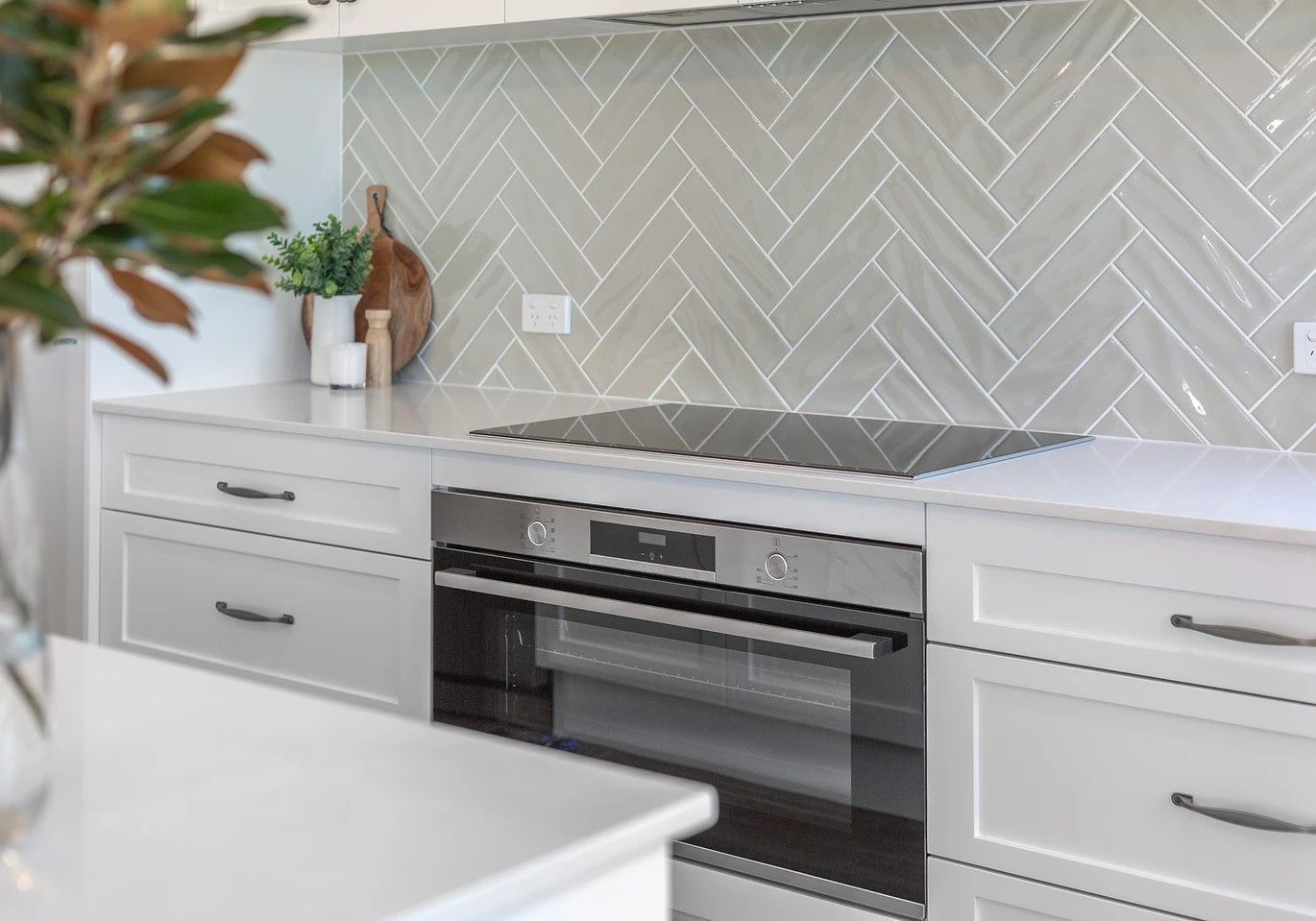 White kitchen with herringbone tile backsplash, integrated oven, and cooktop.