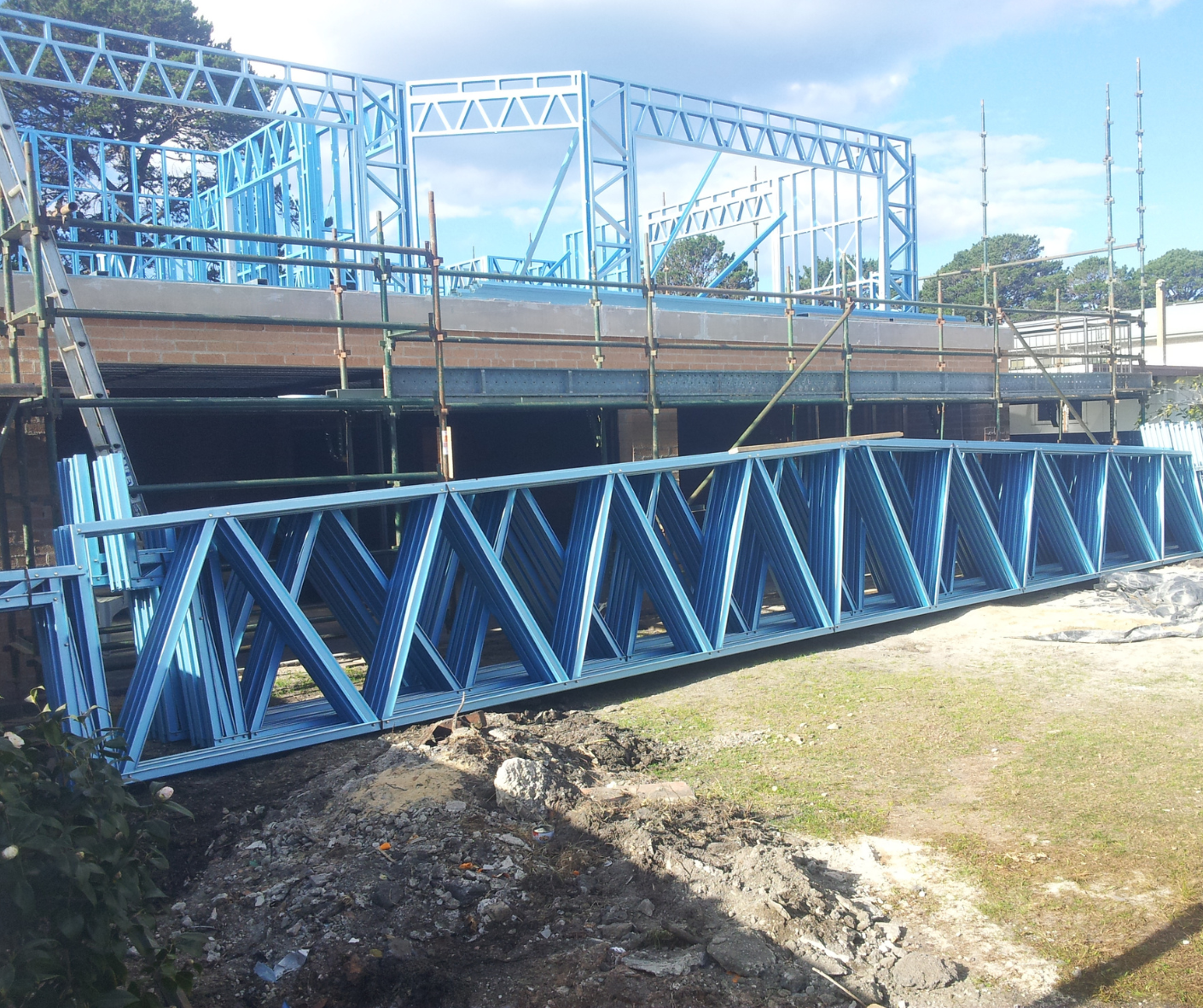 Blue steel truss bridge spanning a dry channel beside a road under a clear sky