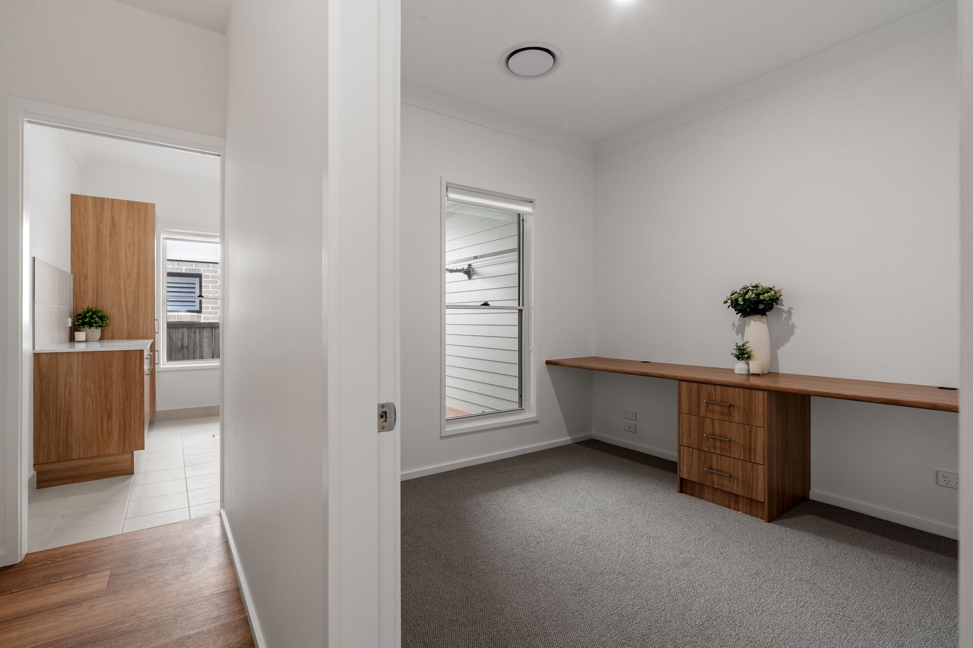 An interior view of a room with a built-in wooden desk, a window, and a door leading to a hallway.