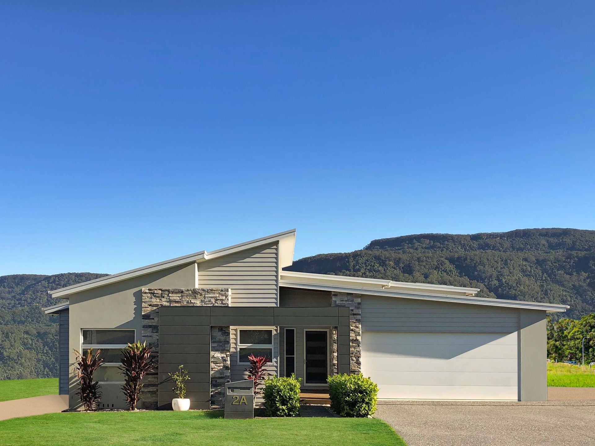 Modern gray house with stone accents, a sloped roof, and attached garage in front of a mountain range.