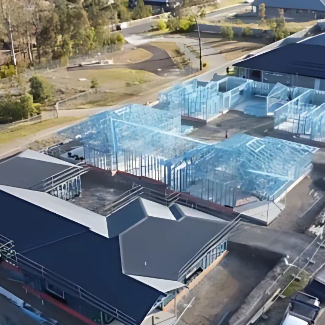 Aerial view of a building under construction, featuring blue steel framing and dark gray roofs.
