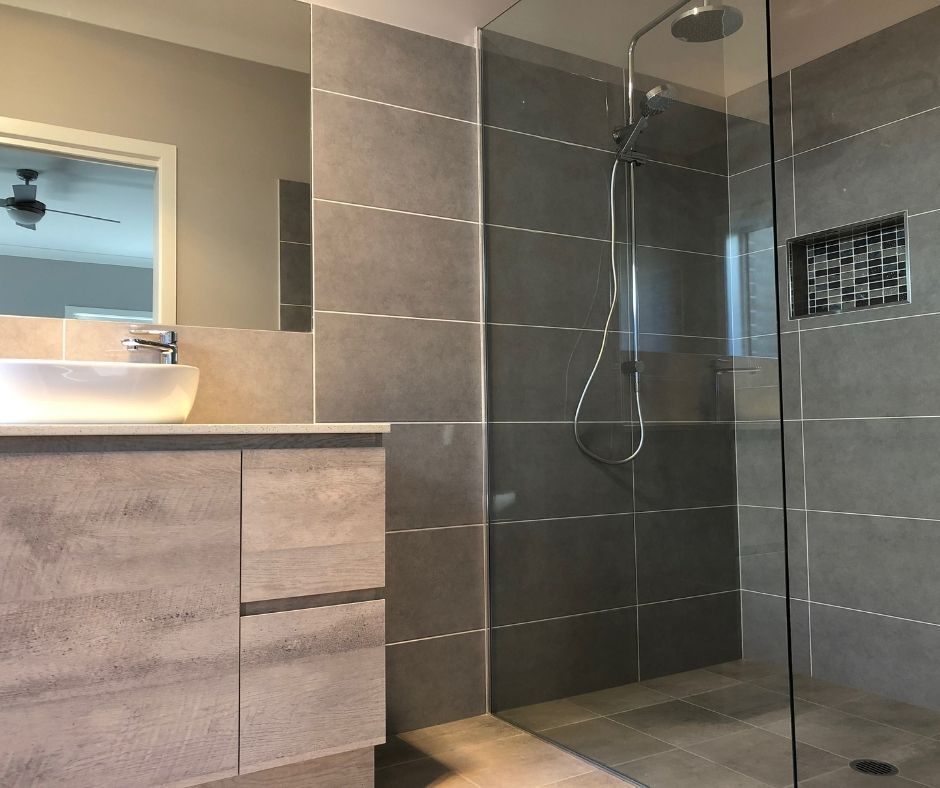 Gray-tiled modern bathroom with glass shower, floating vanity with vessel sink, and recessed mosaic tile niche.