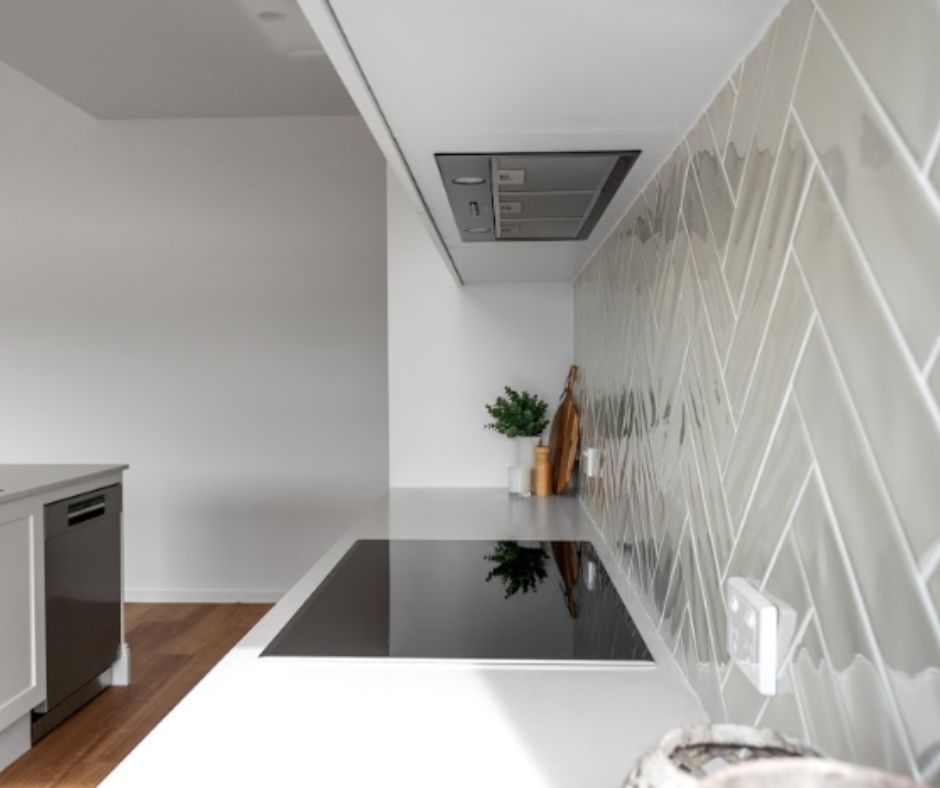 Modern kitchen with white countertop, black cooktop, tiled backsplash, and built-in range hood.