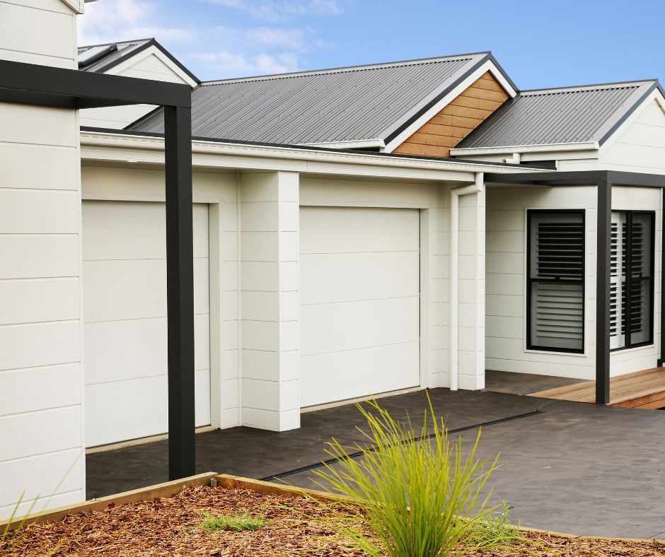 Modern single-story house exterior with white garage doors, gray roof, and landscaped front yard