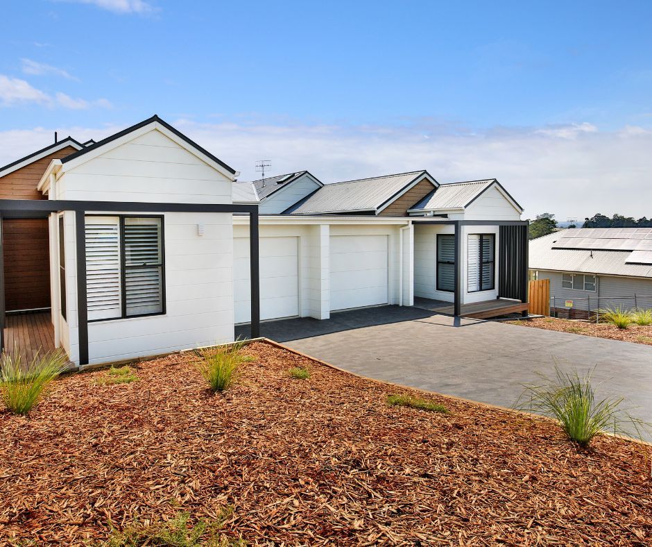 Modern white single-story house with black trim, garage, and paved driveway in a landscaped yard.