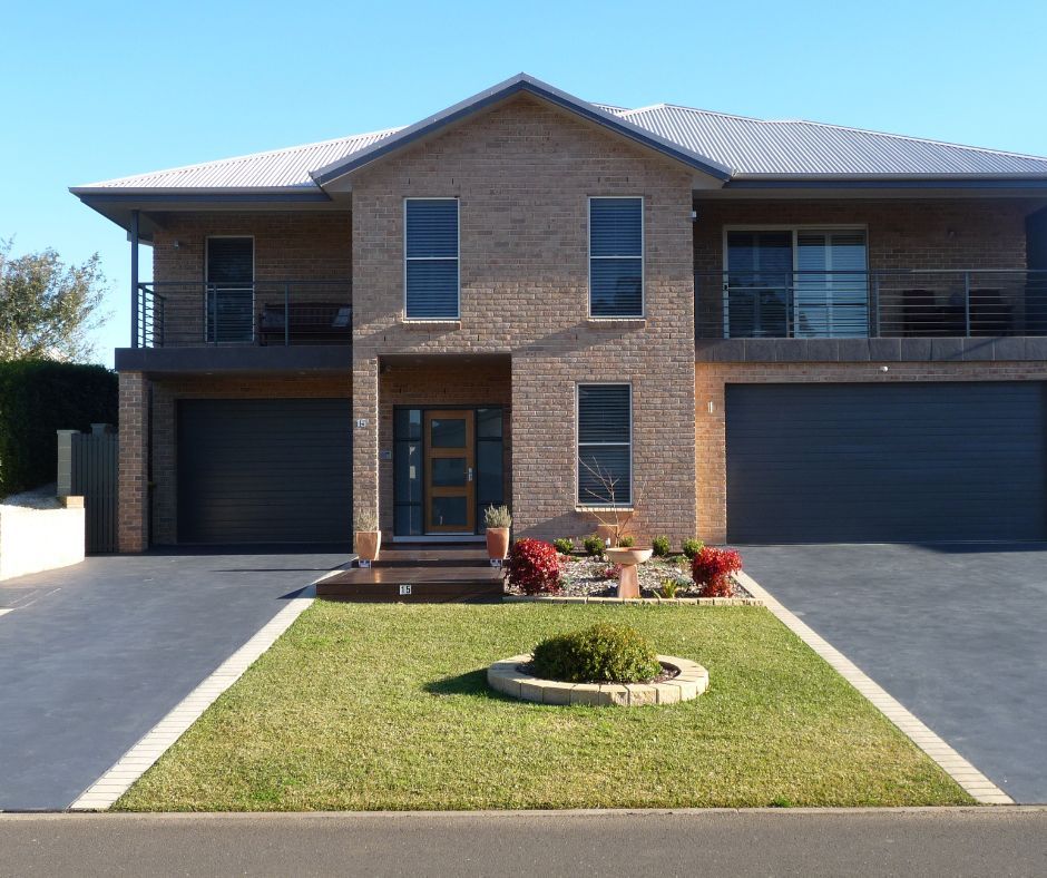 Two-story brick house with double garage, central front door, and a small lawn and driveway in front.