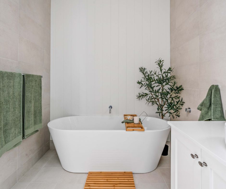 Bathroom with white oval bathtub, olive green towels, wooden bath caddy and plant, and neutral tile walls.