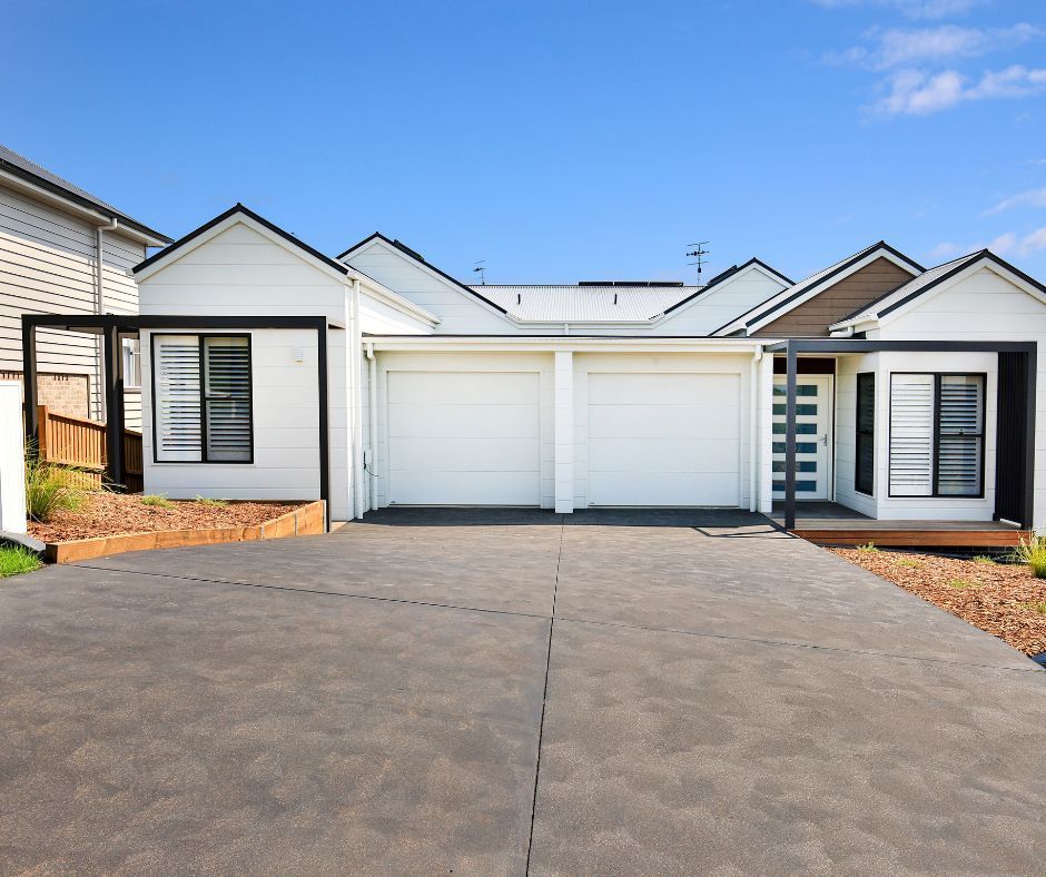 Modern single-story house with white facade, double garage, and wide driveway under a blue sky