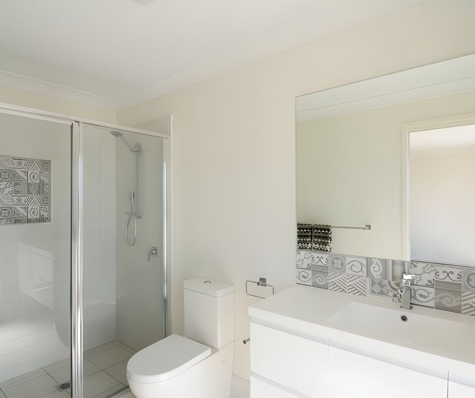 Bathroom with a white toilet, shower, vanity, and mirror, featuring decorative tiles.