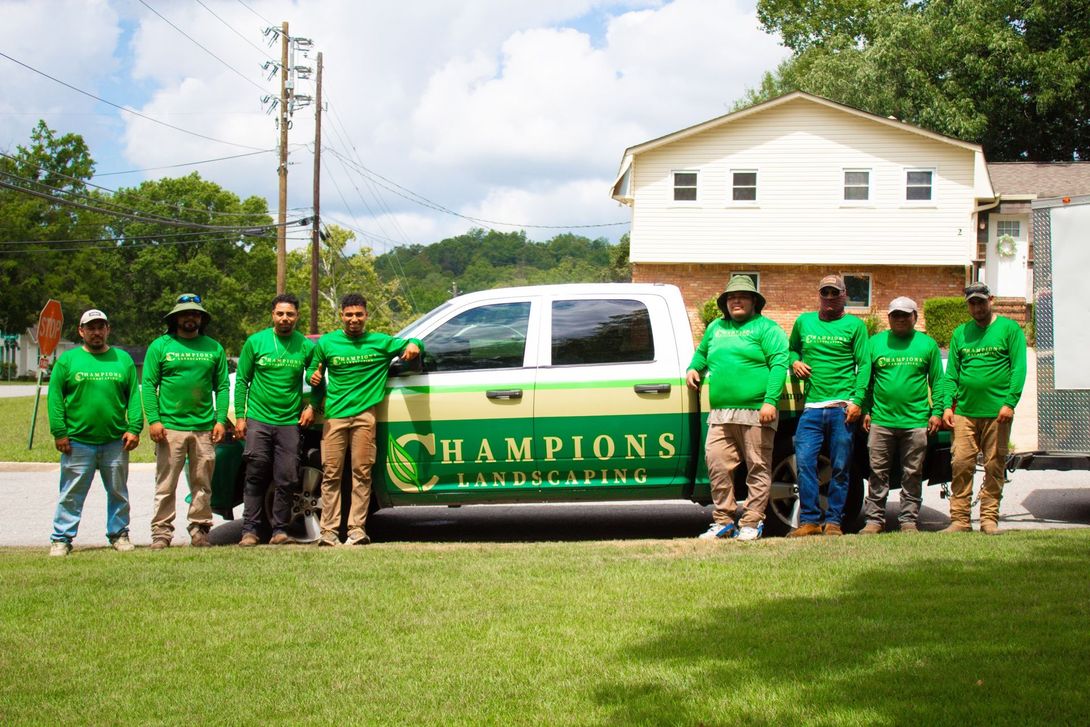 Green-clad team posing beside a white-and-green Champs van on a grassy roadside.