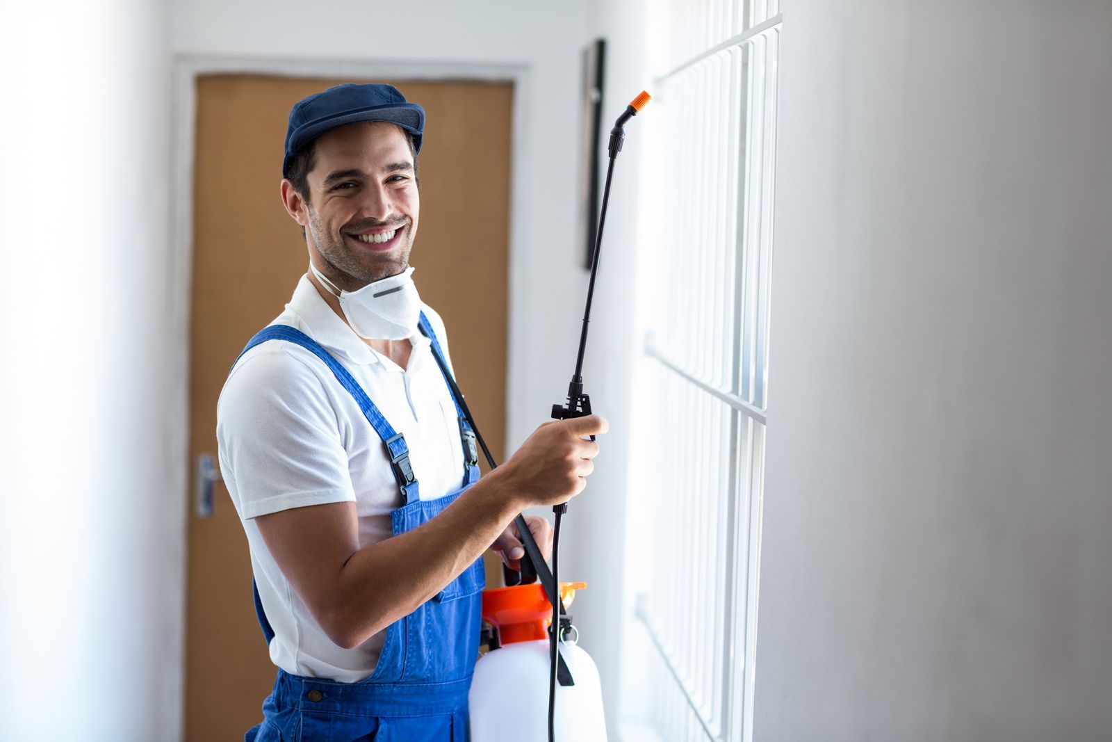 A man wearing a mask is spraying a wall with a sprayer.