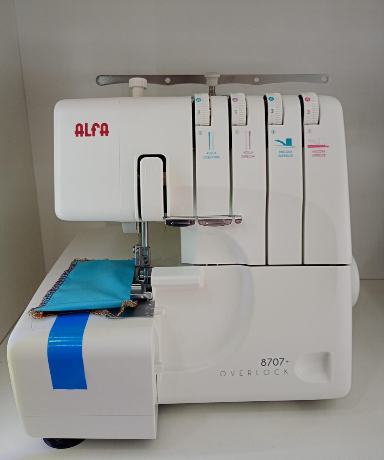 Maquina de coser overlock Alfa color blanco con tela color turquesa.