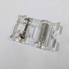 Un prensatelas de plástico transparente para máquina de coser con rodillo metálico y barra de fijación