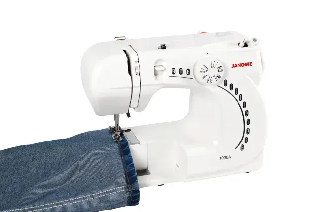 Una máquina de coser Janome blanca sobre un fondo blanco, con selectores de puntada y mecanismo de aguja.