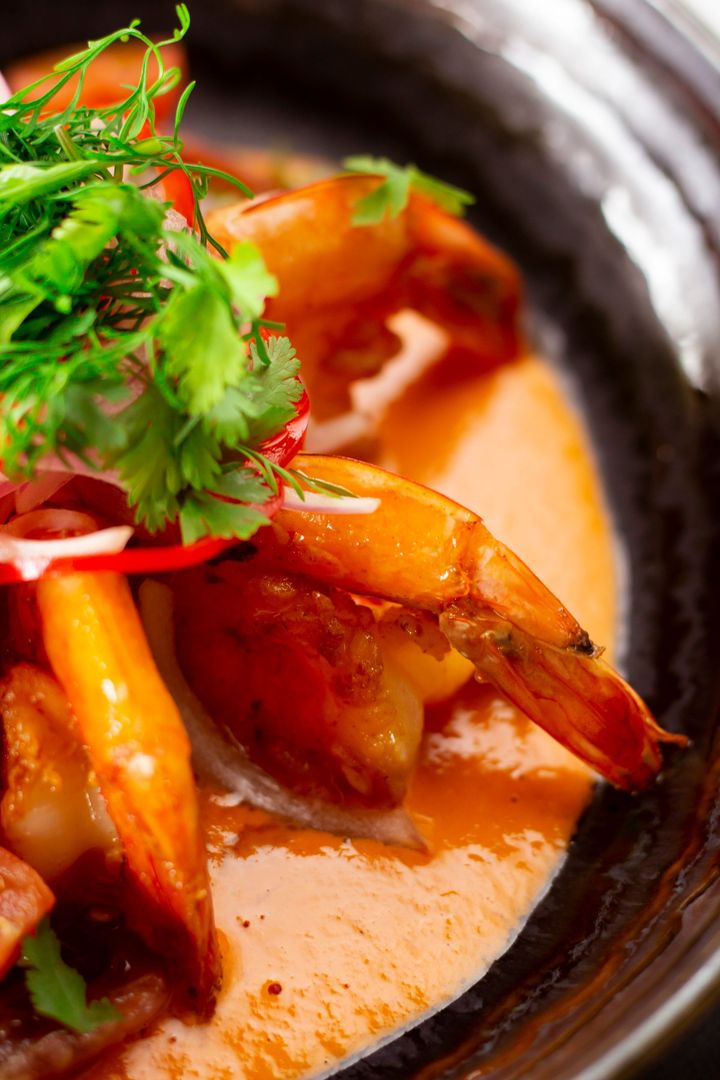 Shrimp in a sauce, garnished with cilantro and radish, in a dark bowl.