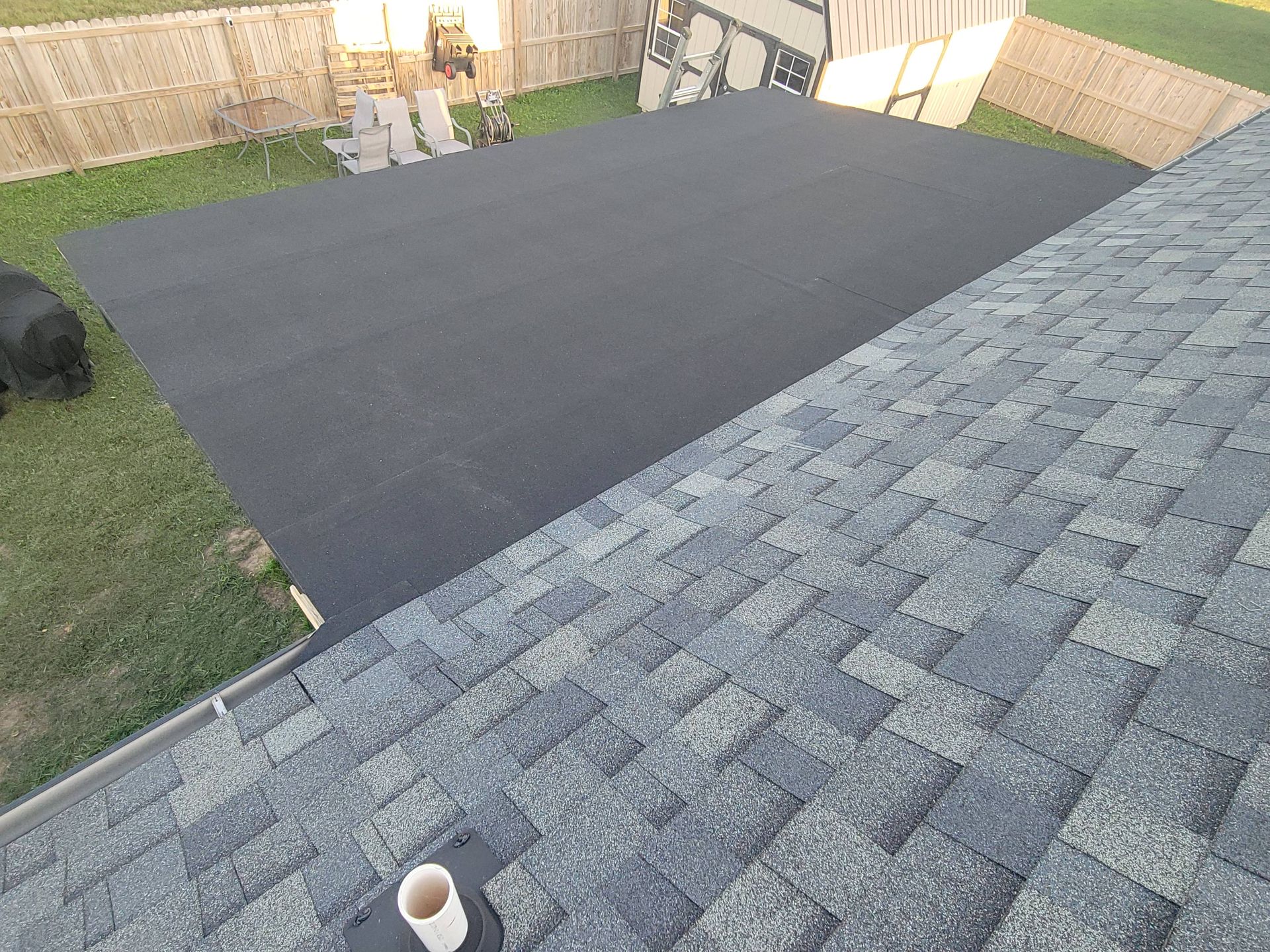 Overhead view of a black tarp covering a backyard, adjacent to a house with a gray shingle roof.