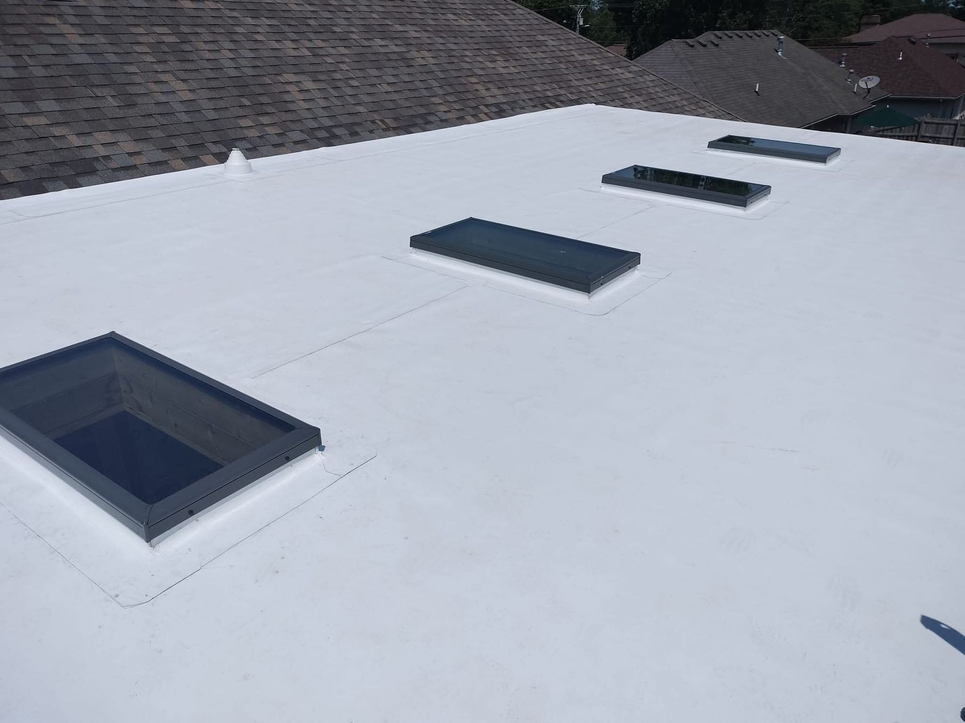 White flat roof with four dark rectangular skylights near shingled roof edges White flat roof with four dark rectangular skylights near shingled roof edges