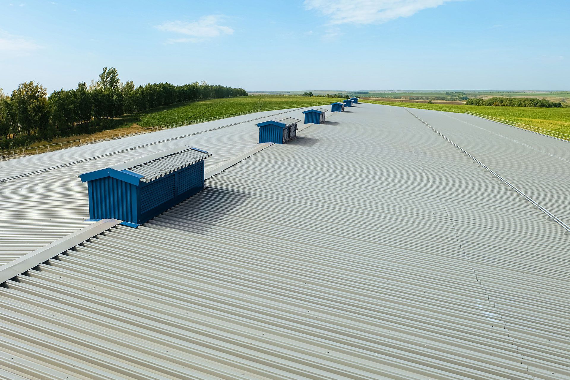 Blue-roofed structures on a large, textured gray surface, under a blue sky, surrounded by green fields.