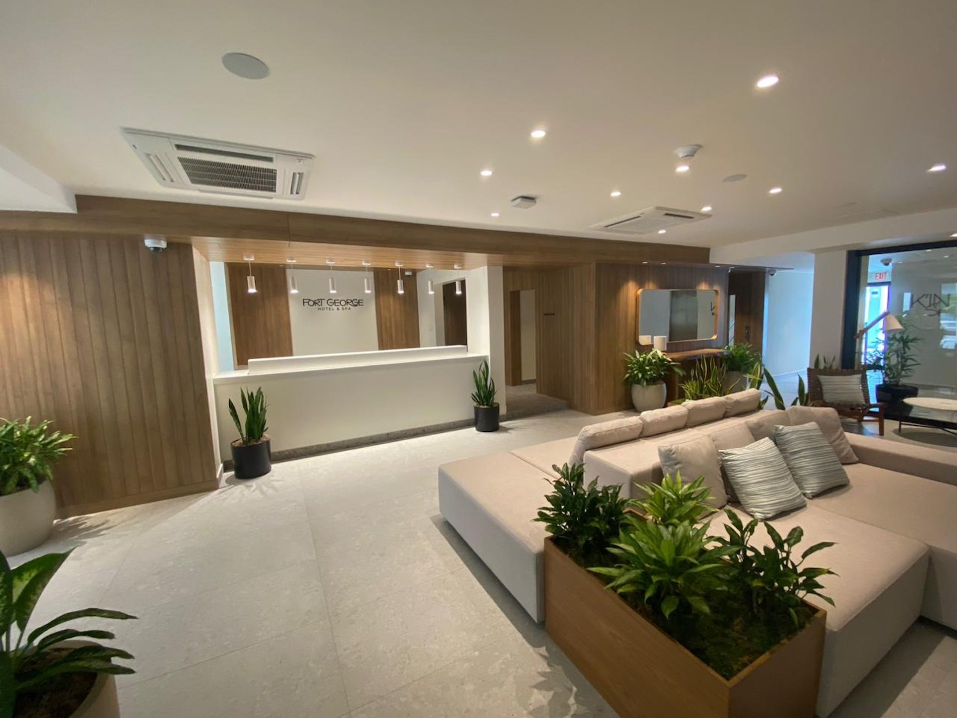 Modern hotel lobby with a reception desk, beige seating, potted plants, and warm wood accents
