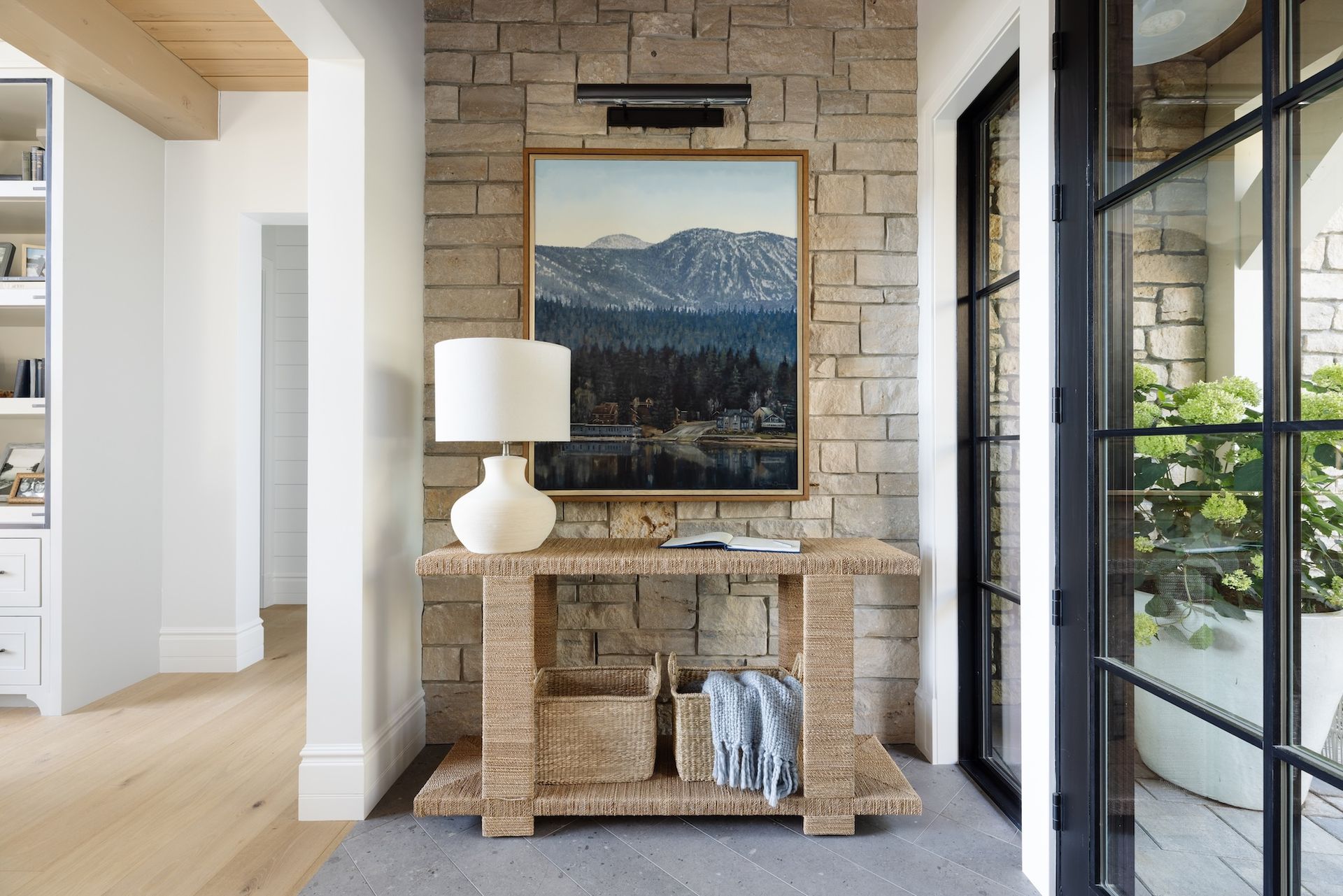 Stone fireplace with a framed landscape, white lamp, and console table in a bright modern hallway