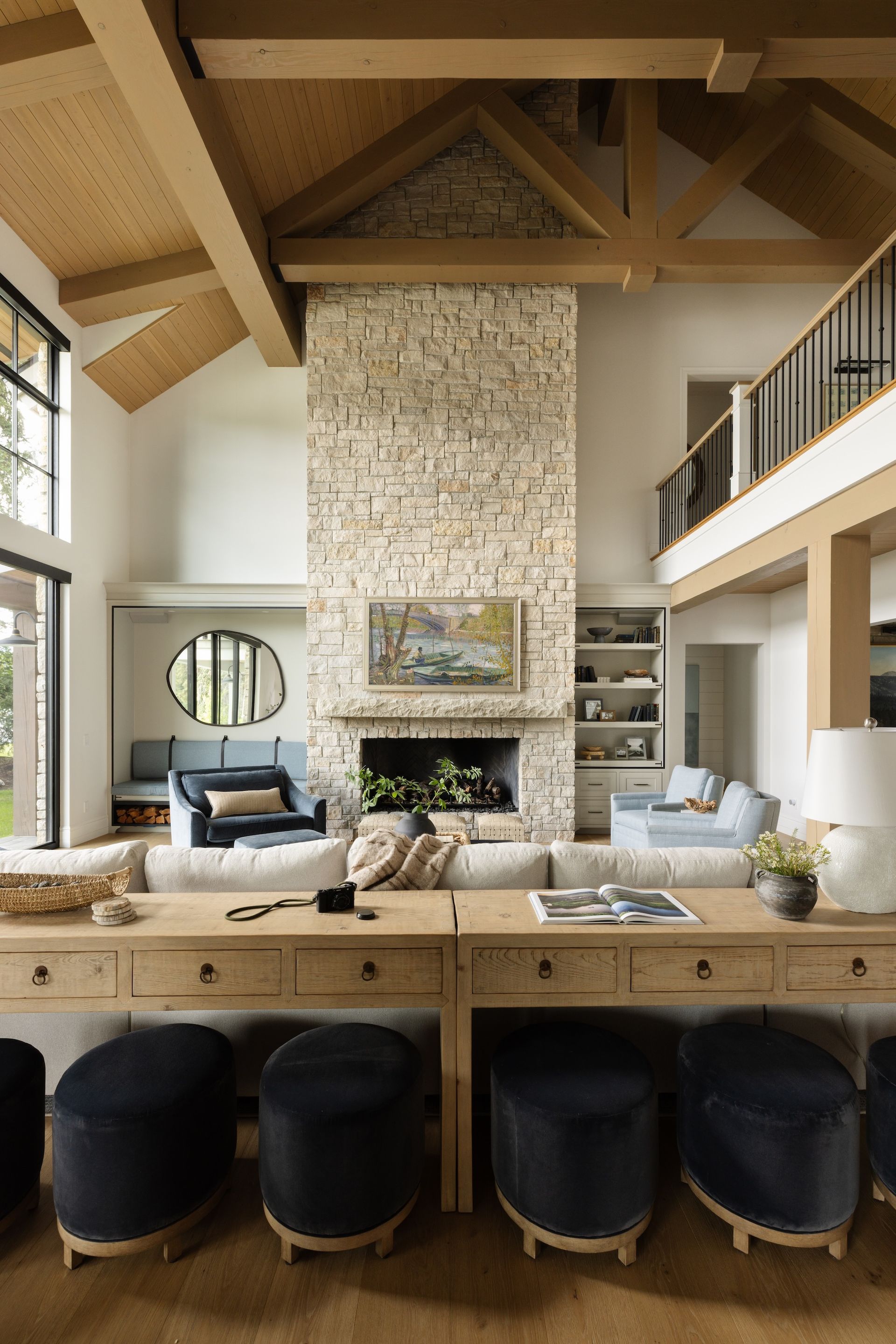 Open-concept living room with stone fireplace, vaulted wood ceiling, and leather stools at a kitchen island