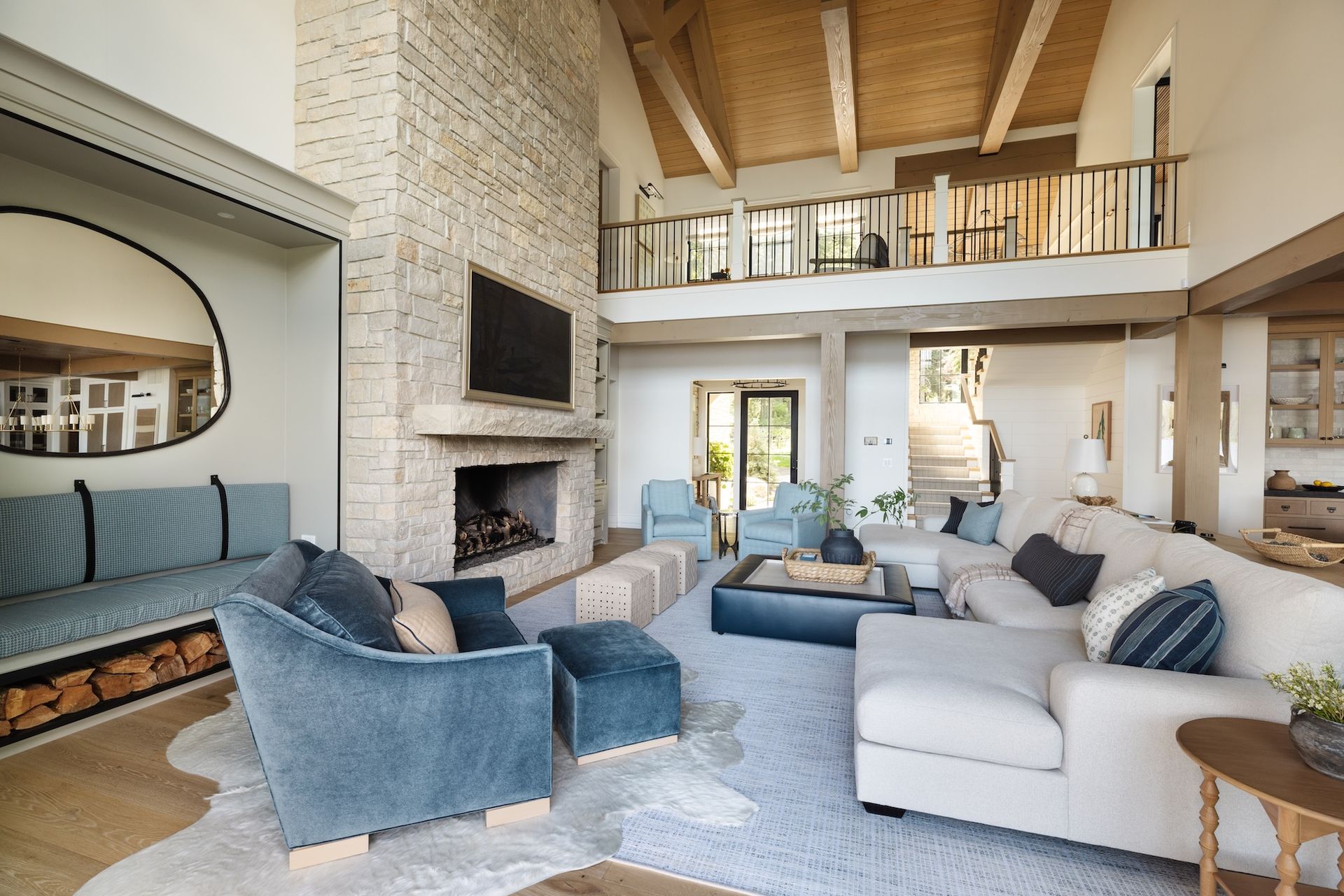Spacious modern living room with vaulted wood ceiling, stone fireplace, blue chairs, and light sofas