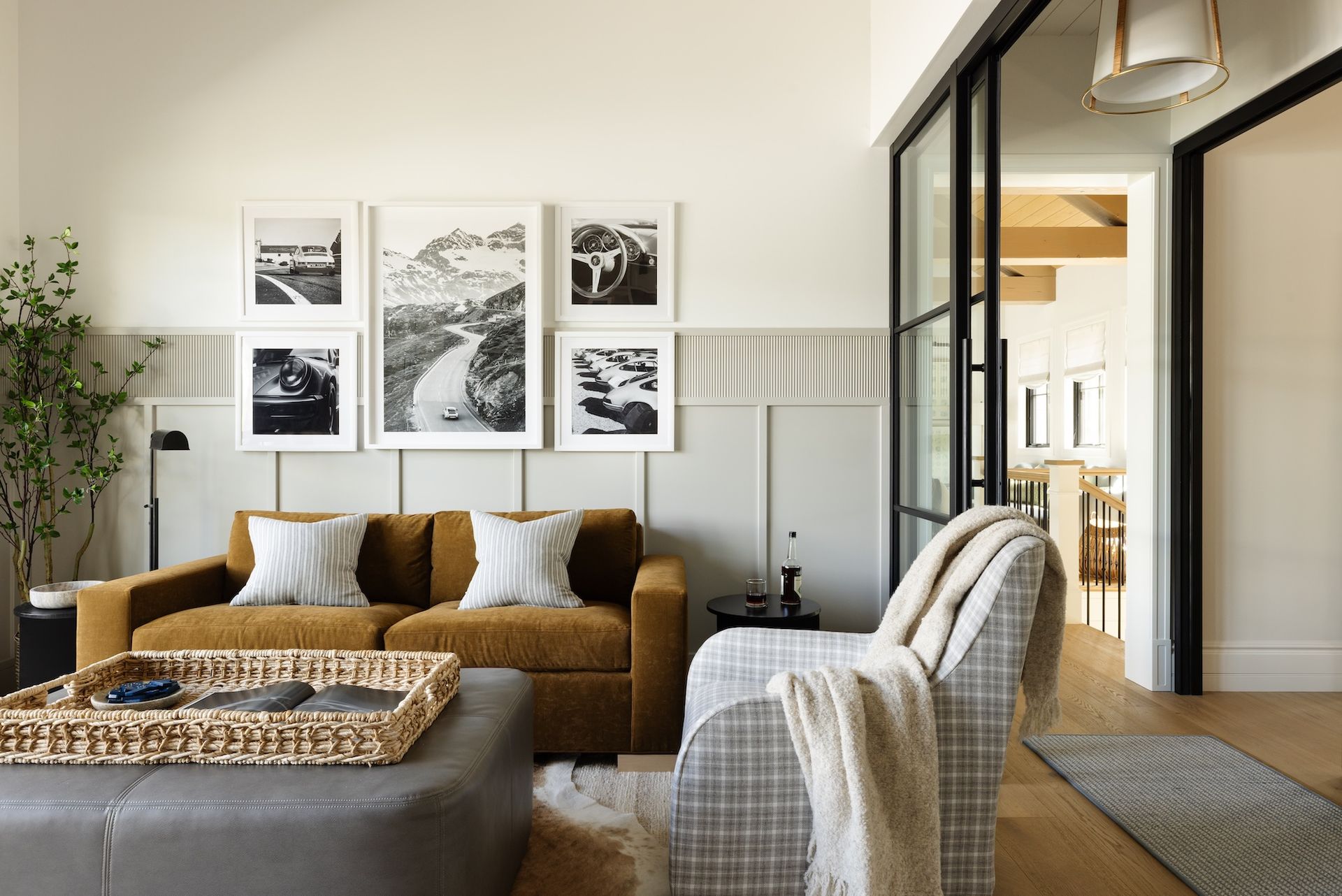 Cozy living room with tan sofa, plaid armchair, coffee table, gallery wall, and open doorway to another room