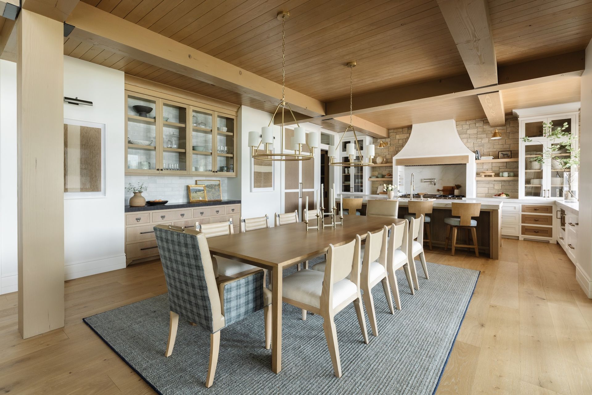 Bright dining room with wooden table, chairs, large windows, and fireplace in a modern cabin-style interior