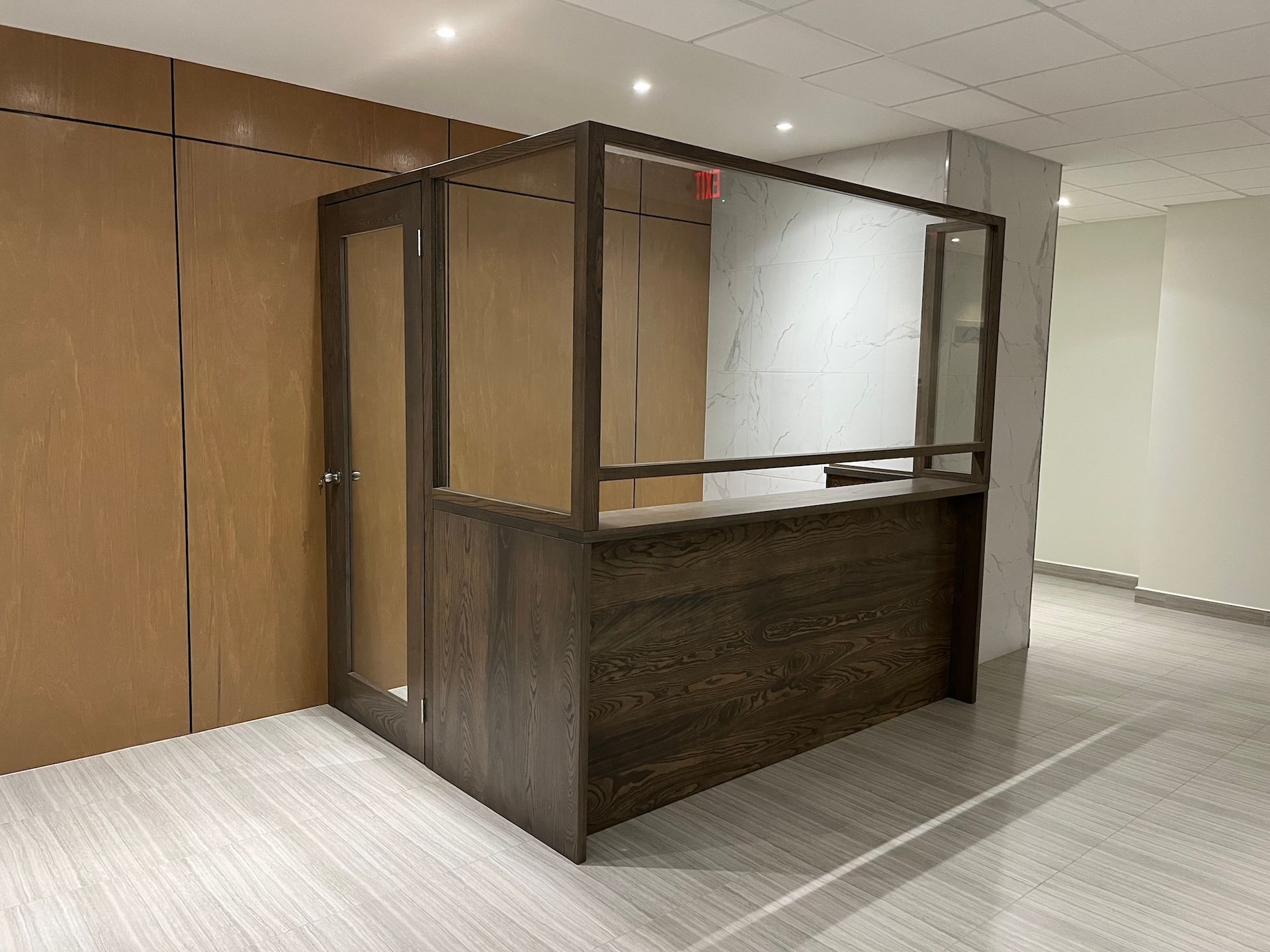 Empty reception desk in a modern hallway with wood paneling and glass partitions.