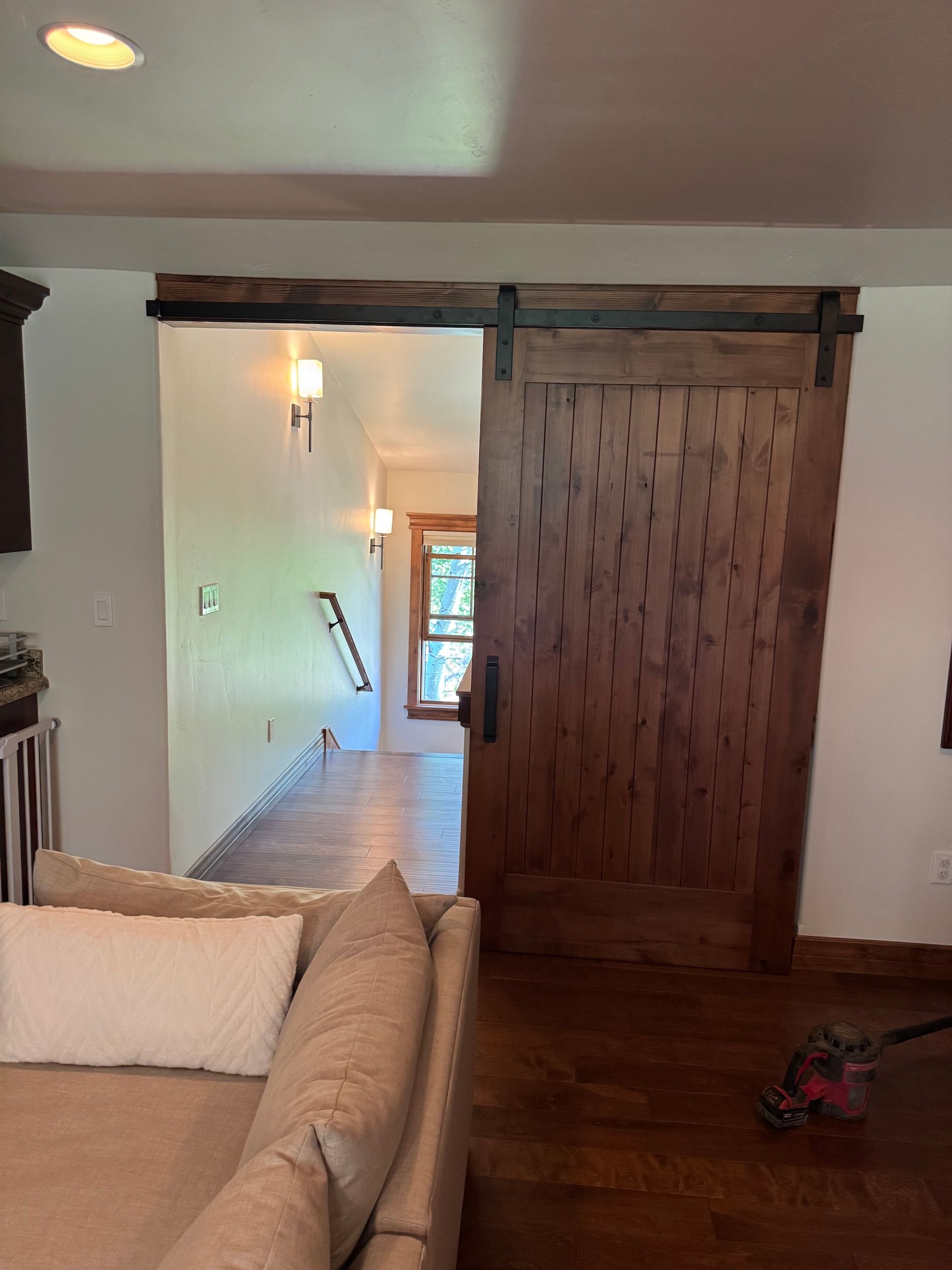 Living room with beige sofa, dark wood barn door, and hallway leading to a bright window