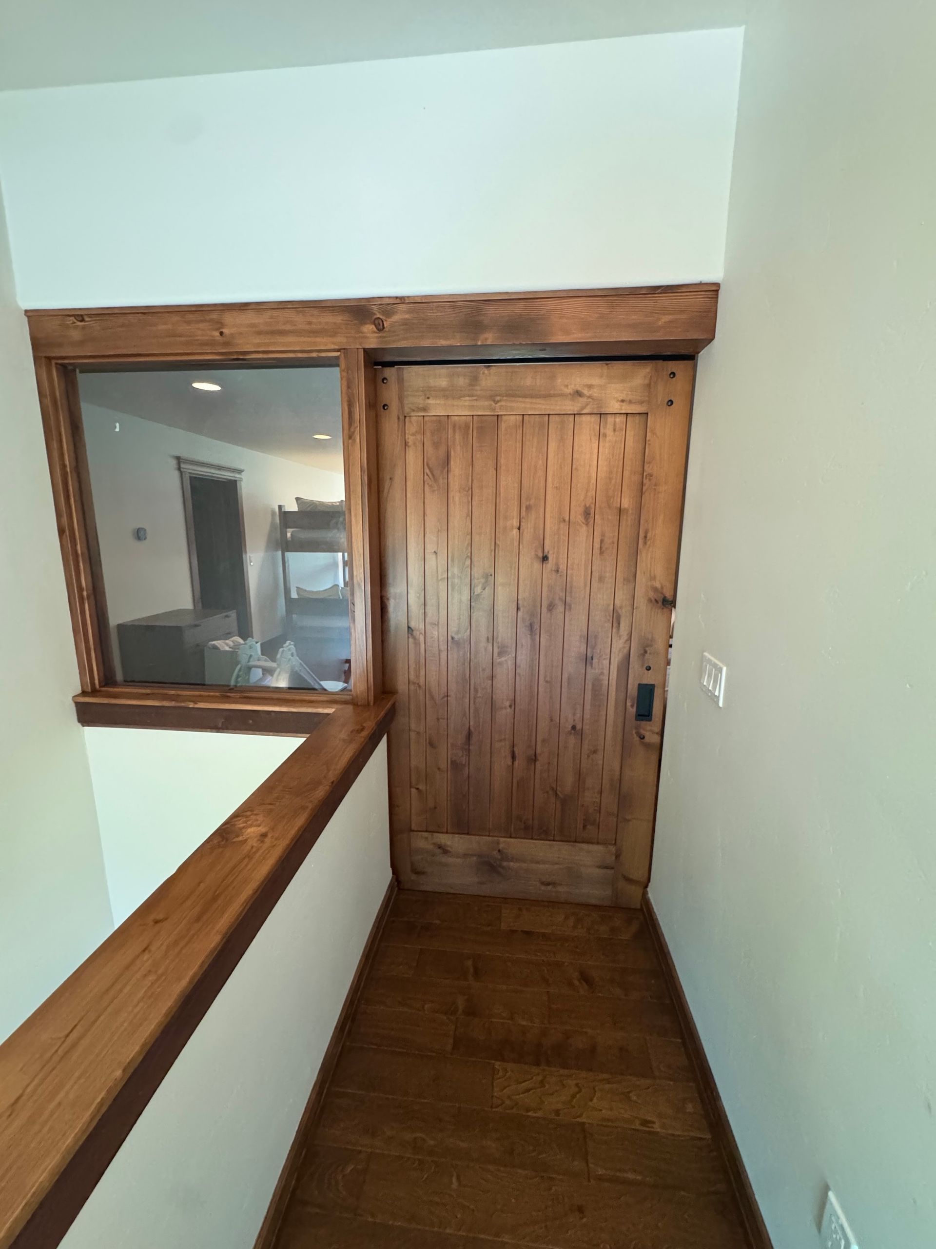 Narrow hallway with wood trim, railing, and a wooden door at the end
