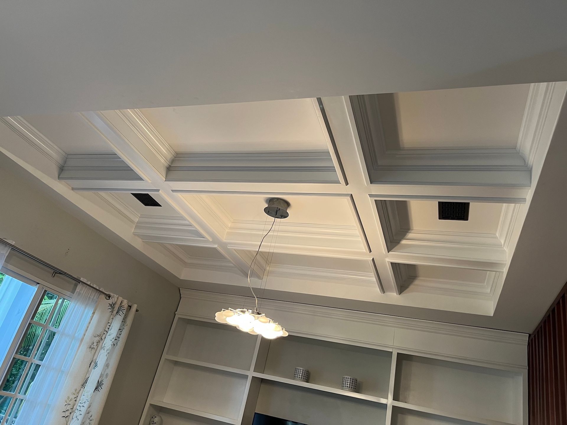 Ceiling with decorative panels, recessed lights, and a hanging light fixture above a room bookshelf
