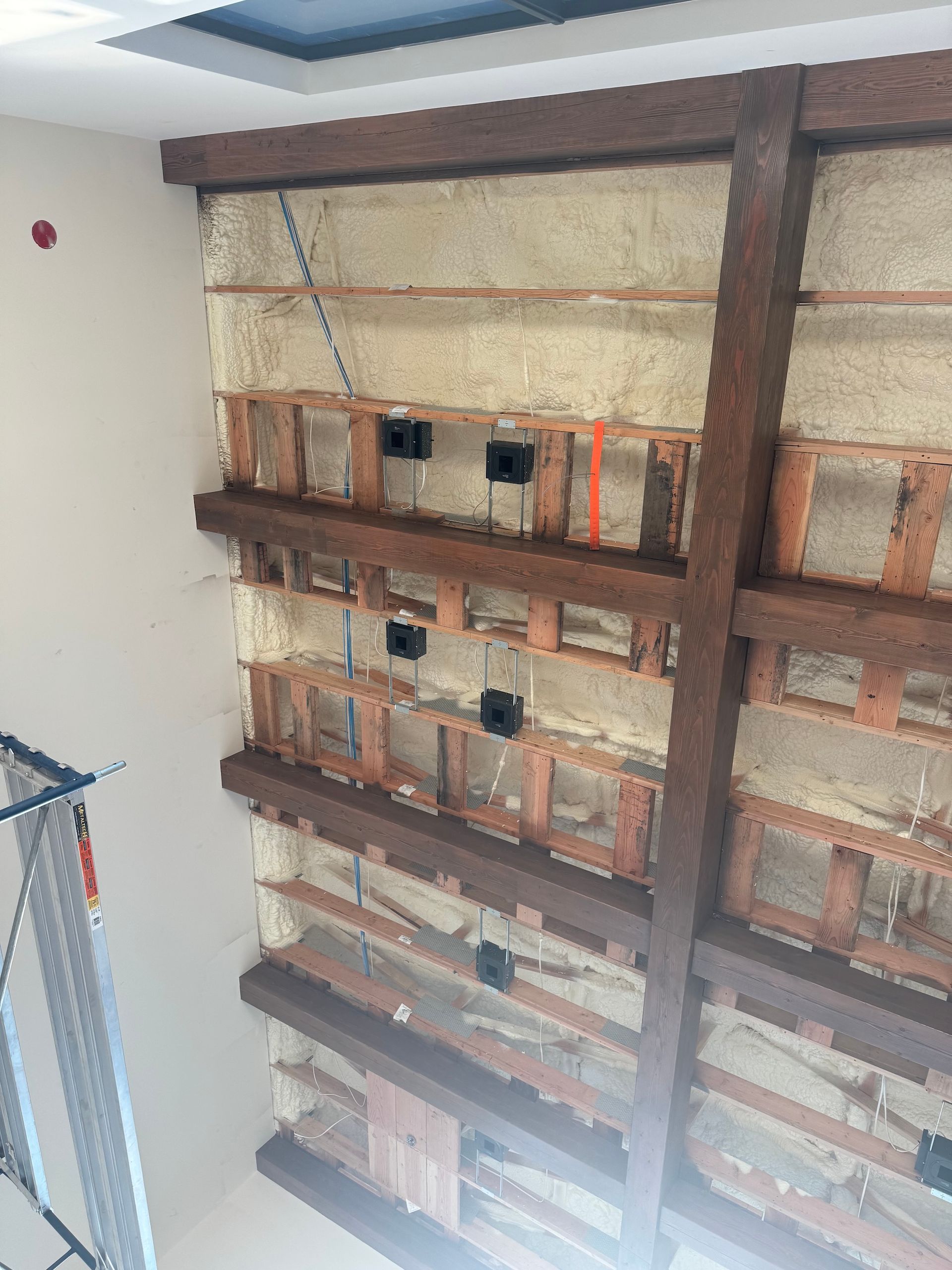 Construction site interior with exposed brick wall, wooden beams, and a hanging cable by a window.